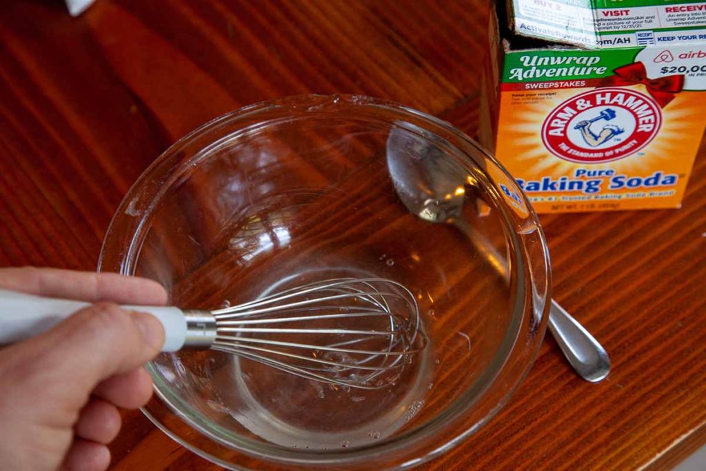 Image of a bowl with water and baking soda being whisked together
