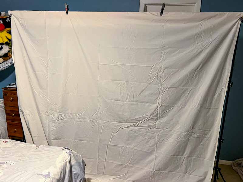 a white sheet hanging on a board propped on two light stands