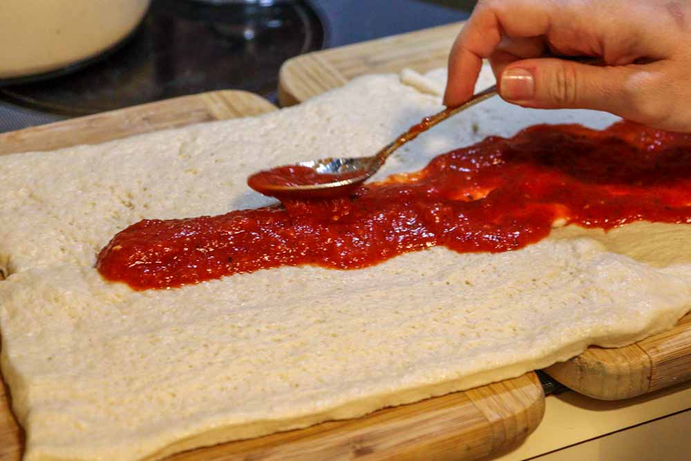Tomato sauce being spread on pizza dough